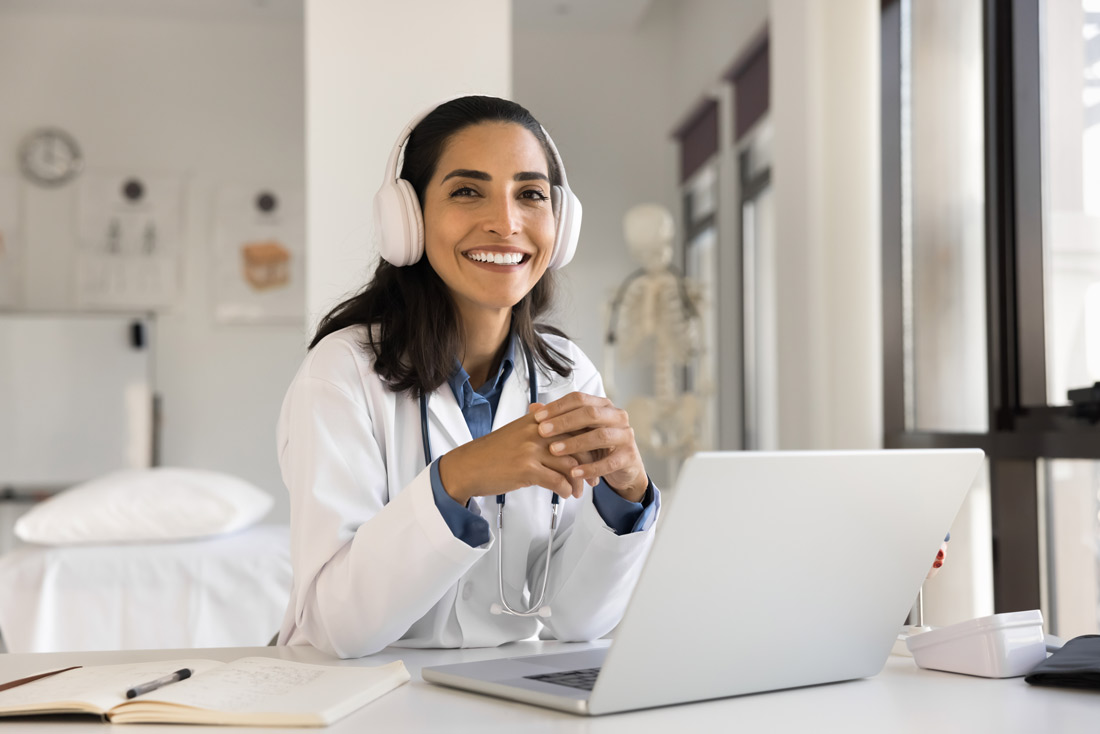 A middle aged woman is smiling wearing casual clothing and holding an ipad. She is surrounded by older women who seem to be enjoying an exercise program outdoors with her as the leader.
